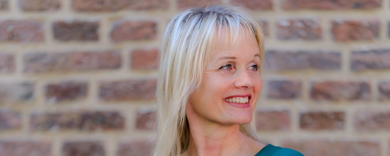 Portretfoto van monique krol voor een bakstenen muur met de tekst monique krol organisatie & communicatie