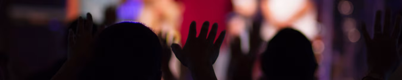 Organisatie bijeenkomst met handen omhoog in aanbidding en betrokkenheid in een donkere zaal sfeer van gemeenschap