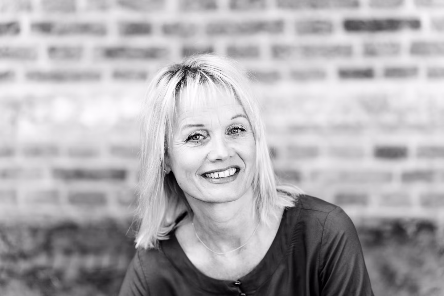 Portretfoto in zwart-wit van monique krol voor een bakstenen muur bij over monique
